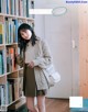 A woman standing in front of a bookshelf holding a white bag.