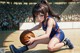 A woman kneeling on a basketball court holding a basketball.